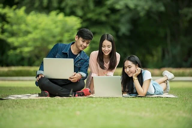 Pessoas Sorrindo juntas com notebook na grama